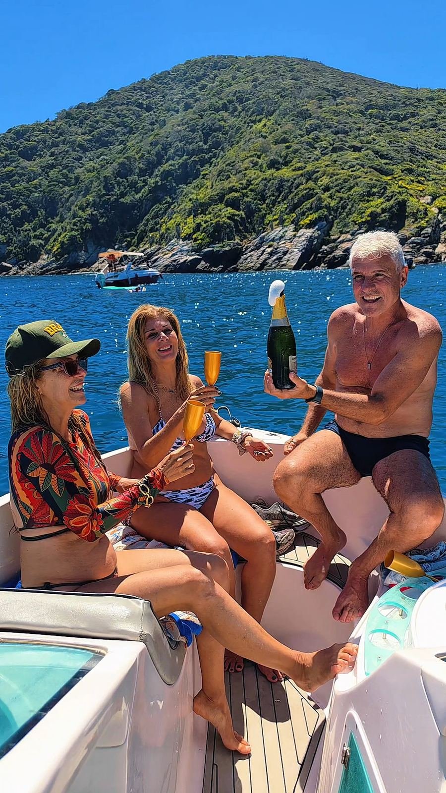 Amigos brindando a bordo, com o morro verde ao fundo