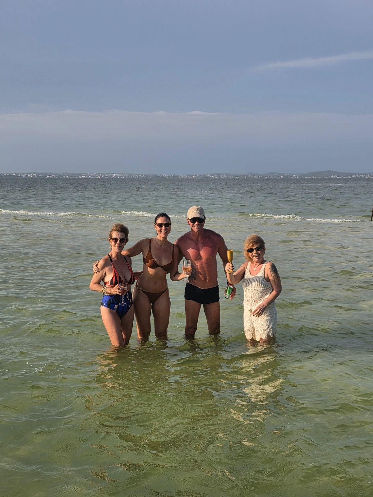 Grupo de amigos com taças em pé na água rasa da lagoa
